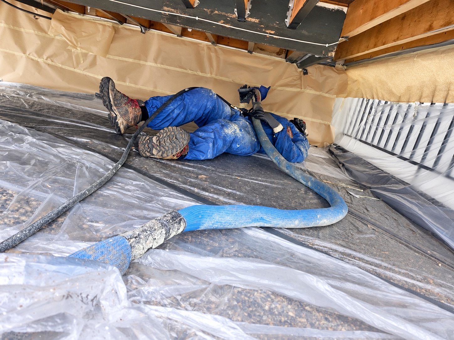 Installer and hose beneath timber floor joists in a protected low-clearance work area