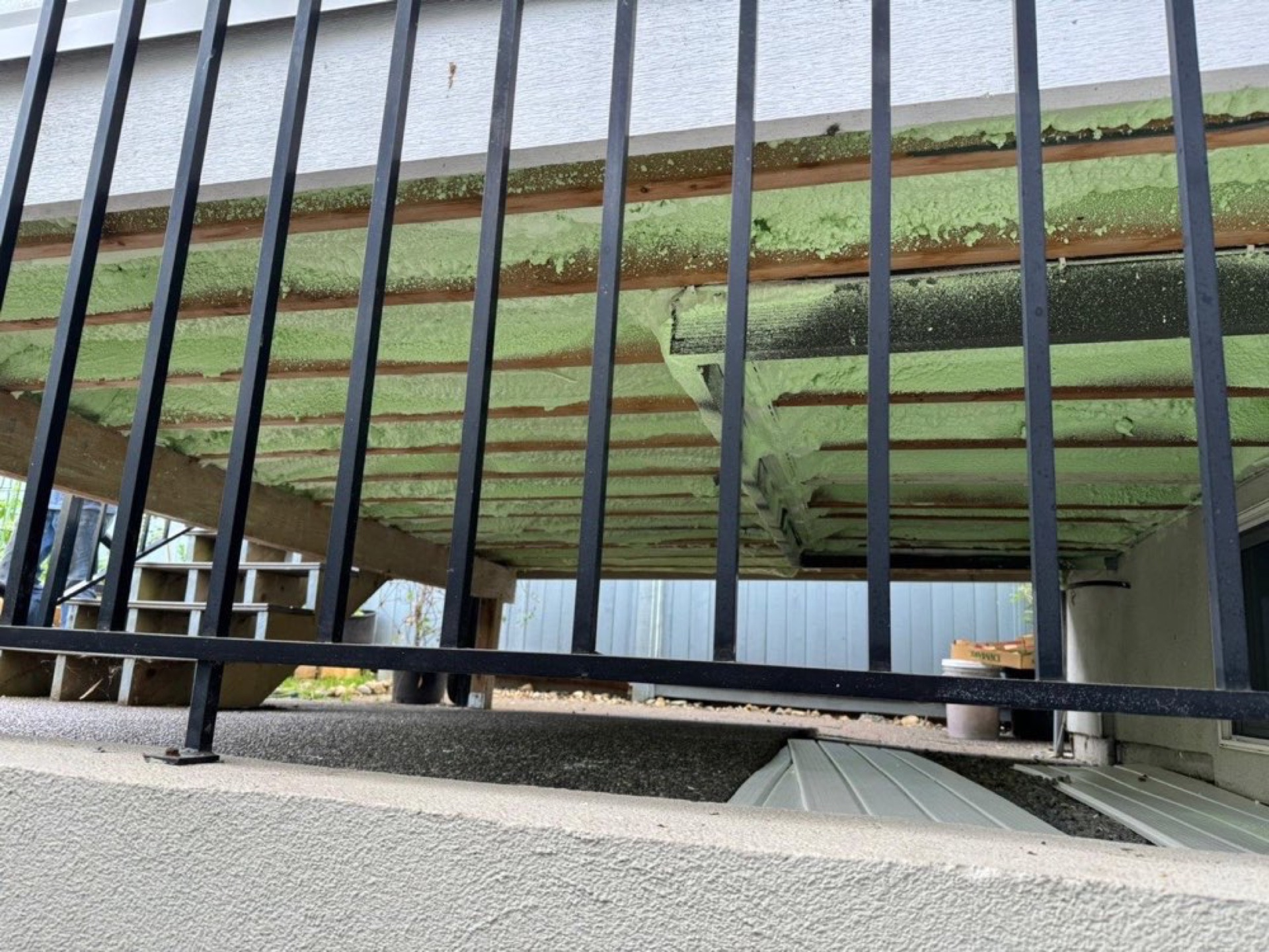 Green-coloured foam visible between timber members beneath an elevated floor, viewed through a railing.